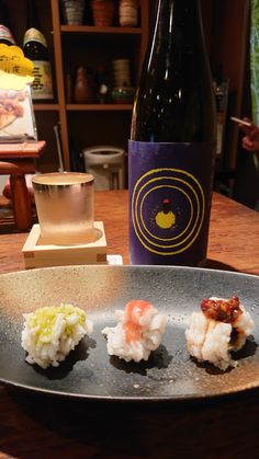 three sushi on a plate next to a bottle of wine