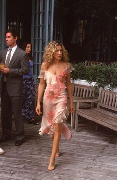 a woman in a pink dress walking down a wooden walkway next to a man in a suit