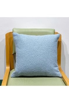 a light blue pillow sitting on top of a green chair next to a white wall