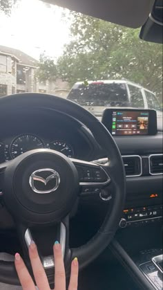 a woman driving a car with her hand on the steering wheel while holding a cell phone