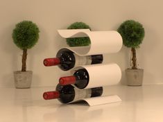 three wine bottles are stacked on top of each other in front of two potted trees