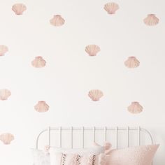 a white bed topped with pink pillows next to a wall covered in seashells