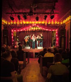 a group of people sitting in front of a stage with lights on the ceiling and chairs