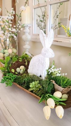 a wooden tray filled with fake eggs and greenery on top of a white table