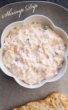 a white bowl filled with dip next to crackers on top of a gray surface