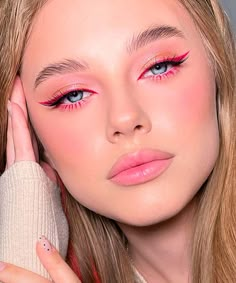 a woman with pink eye makeup holding her hand up to her face and looking at the camera