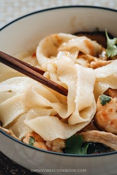 a white bowl filled with shrimp and dumplings next to chopsticks in it