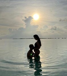 a woman and child are in the water at sunset, with the sun behind them