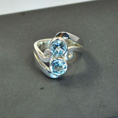 Sterling silver ring with blue topaz settings, available in the following sizes: U.K. sizes: N, O, Q, S. U.S. sizes: 7, 7 ½, 8 ½, 9 ½. DO NOT FORGET TO GIVE YOUR FINGER SIZE WHEN SENDING THE ORDER. The gemstones are good quality, the settings are done by hand and there is a brilliant polished finish.  Technical details: stones sizes 6mm/0,24 inch. Total ring width including stones and silver: 19mm/0,75 inch. Thickness of shank: 1,2mm/0,05 inch. Formal Sterling Silver Topaz Birthstone Ring, Modern Blue Topaz Round Ring, Modern Blue Topaz Ring, Round Shape, Formal Silver Crystal Ring With Blue Topaz, Anniversary Silver Topaz Ring With Accent Stones, Silver Blue Topaz Crystal Ring For Formal Occasions, Modern Round Blue Topaz Ring, Gift Blue Topaz Ring With Polished Finish, Blue Topaz Open Ring For Anniversary