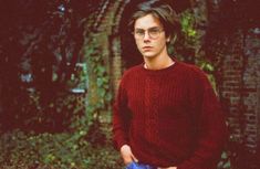 a man with glasses standing in front of some trees and bushes, holding a blue frisbee