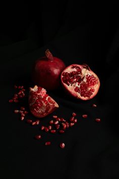 two pomegranates and seeds on a black background with one cut in half