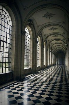 an empty hallway with large windows and black and white checkered flooring on both sides