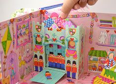 a child's hand is touching the inside of a paper doll house with its door open