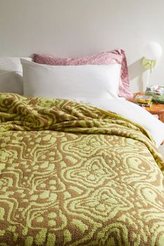 a bed with green and brown bedspread on it next to a night stand