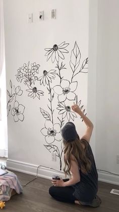 a woman is sitting on the floor with her phone in front of a floral wall decal