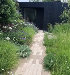 a garden with lots of plants and flowers on the side of the building, along with a brick walkway