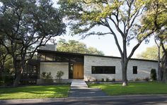 a modern house with large trees in front of it and grass on the side walk