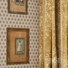 two framed pictures hang on the wall next to a window with gold and blue damask