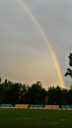 two rainbows in the sky over a field with lawn chairs and trees behind them