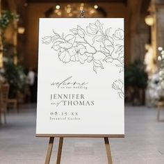 an easel with a wedding sign on it in the middle of a room filled with tables and chairs