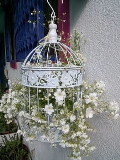 a white birdcage with flowers hanging from it