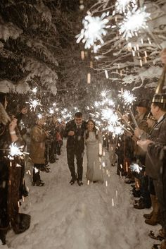 a bride and groom walk through the snow with sparklers in their hands as they leave