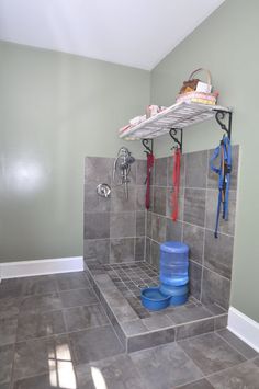 a bathroom with gray tiles and blue buckets on the wall, shelves above it