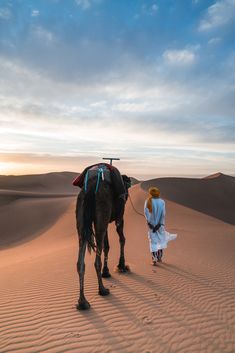 a person walking with a camel in the desert