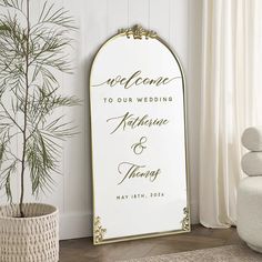 a wedding welcome sign in front of a potted plant on the floor next to a window