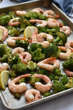 shrimp and broccoli on a baking sheet with lemon wedges