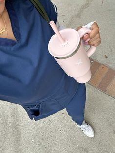 a woman holding a pink coffee cup while sitting on the ground next to a sidewalk