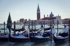 several gondolas are tied to poles in the water near buildings and a clock tower