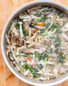 a bowl filled with noodles and vegetables on top of a wooden table