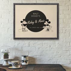 a mickey mouse poster hanging on the wall above a table with coffee cups and mugs