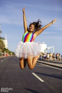 a woman jumping in the air while wearing a tutu and rainbow dress with her arms outstretched