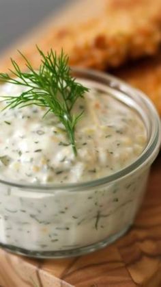 a small glass bowl filled with white sauce and garnished with dill on top