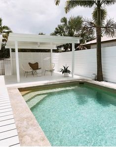 a small swimming pool in front of a white fenced backyard area with palm trees