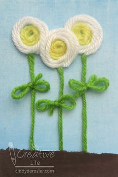 three crocheted flowers with green stems and yellow centers on a light blue background