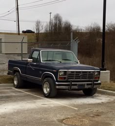 a black truck parked in a parking lot next to a chain link fence and building