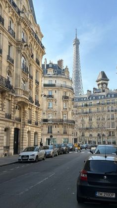 the eiffel tower is seen in the distance from this street lined with parked cars