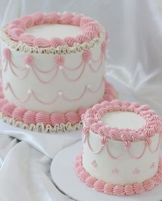 two pink and white cakes sitting on top of a table next to each other in front of a white sheet