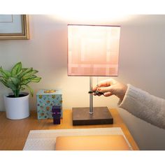 a person holding a remote control in front of a lamp on a wooden table next to a potted plant