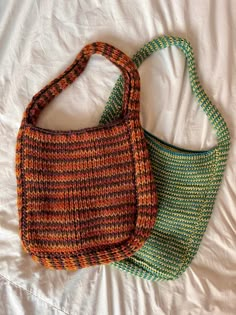 two purses sitting on top of a bed next to each other in different colors