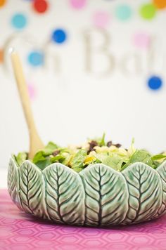 a green leafy salad in a bowl with a wooden spoon on the table next to it