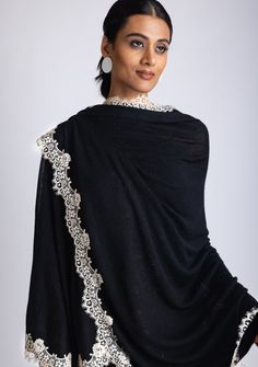 This elegant black knitted cape, crafted from a very soft 100% merino wool, combines warmth and refined designing. The delicate scalloped beige-colored filigree lace border creates a striking contrast against the black wool, adding a touch of sophistication and unique charm. Its soft, free-flowing silhouette makes it a versatile accessory. Whether for daytime outings or evening events, this timeless cape is designed to keep you stylishly cozy while making a bold statement. A must-have piece for Elegant Black Pashmina Shawl For Winter, Elegant Winter Pashmina Shawl, Elegant Cashmere Shawl, Elegant Lace Shawl For Winter, Elegant Winter Lace Shawl, Elegant Black Lace Shawl, Elegant Alpaca Shawl Scarf, Elegant Winter Wool Pashmina Shawl, Elegant Wool Shawl For Winter