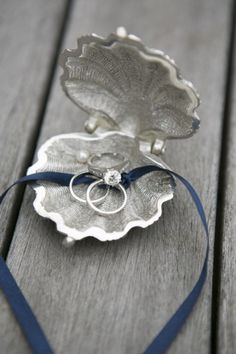 a silver plate with a ring on it sitting on a wooden table next to a blue ribbon