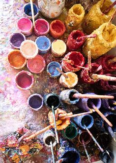 an assortment of paint and brushes sitting on top of a white table covered in lots of different colors