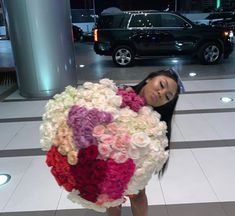 a woman holding a large bouquet of flowers in front of a black car at night