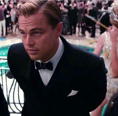 a man in a tuxedo and bow tie sitting next to a pool with people around him