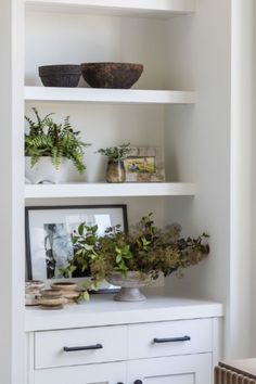 some plants are sitting on top of white shelves in a room with other items and decor